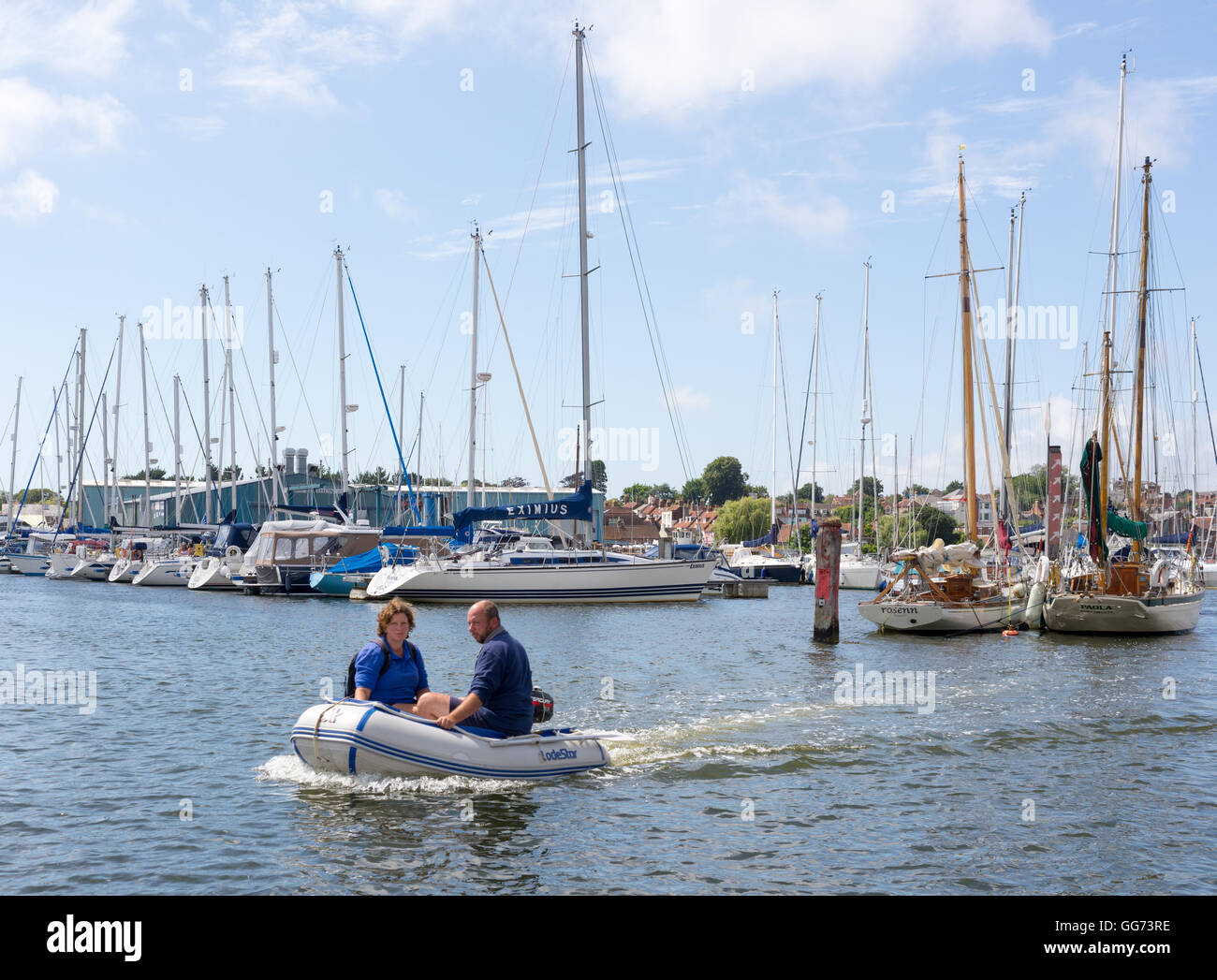 A couple use a dinghy to get to their off-shore moored boat in the sunshine at Lymington Hampshire UK. Stock Photo
