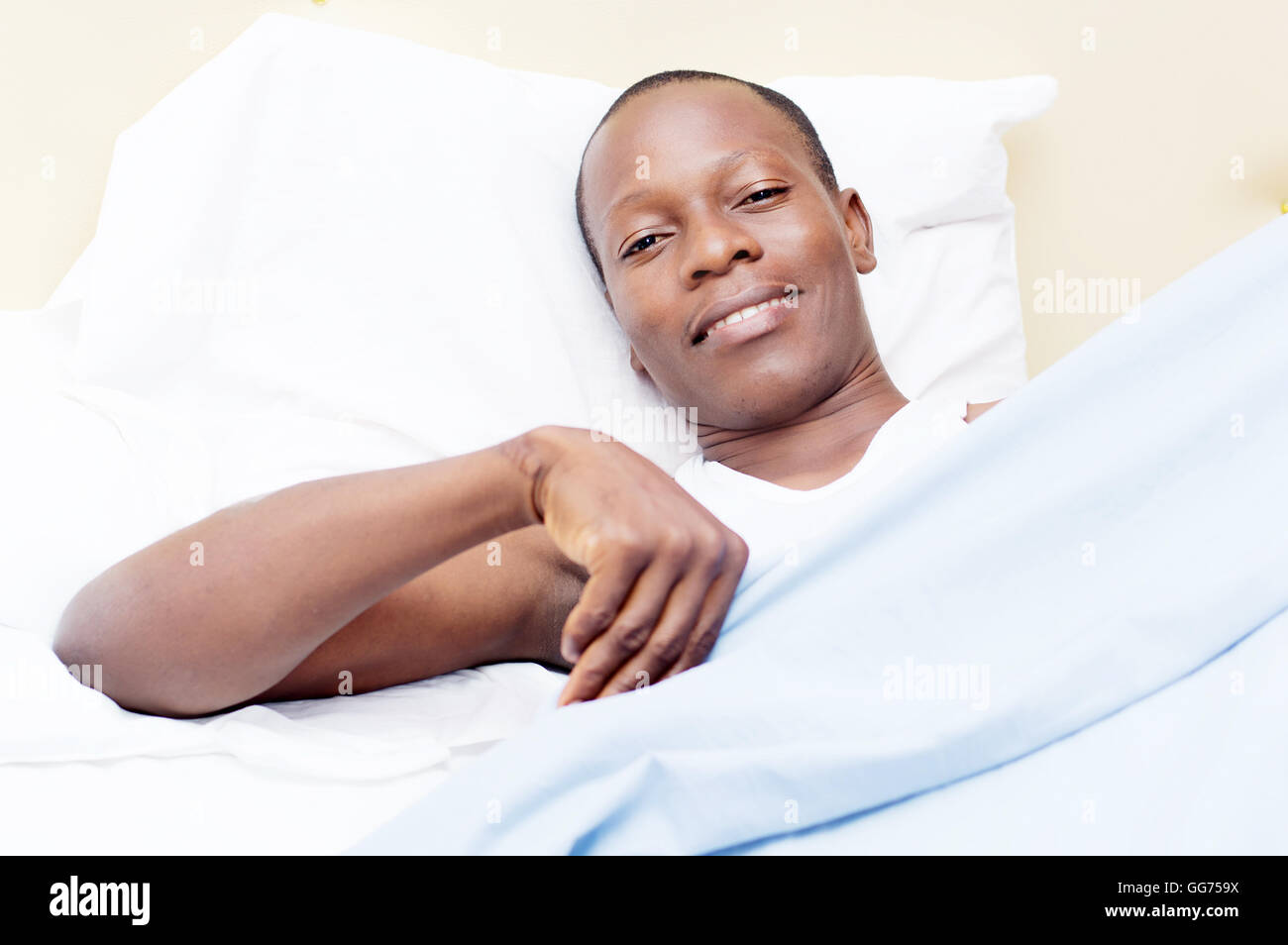 young man lying on a bed, ready to cover smile at the camera Stock