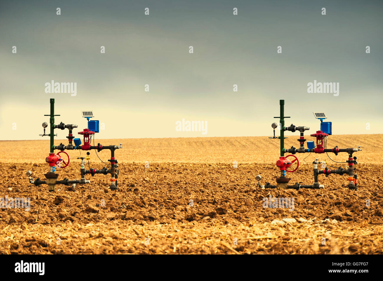 Natural gas wellheads close together in a plowed cornfield. Stock Photo