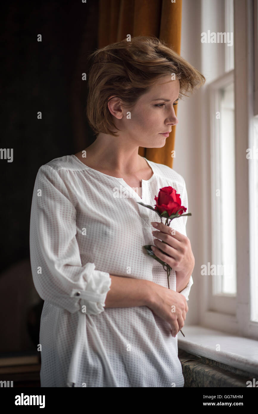 looking-wistfully-out-of-the-window-clutching-a-a-rose-and-waiting-GG7MHM.jpg