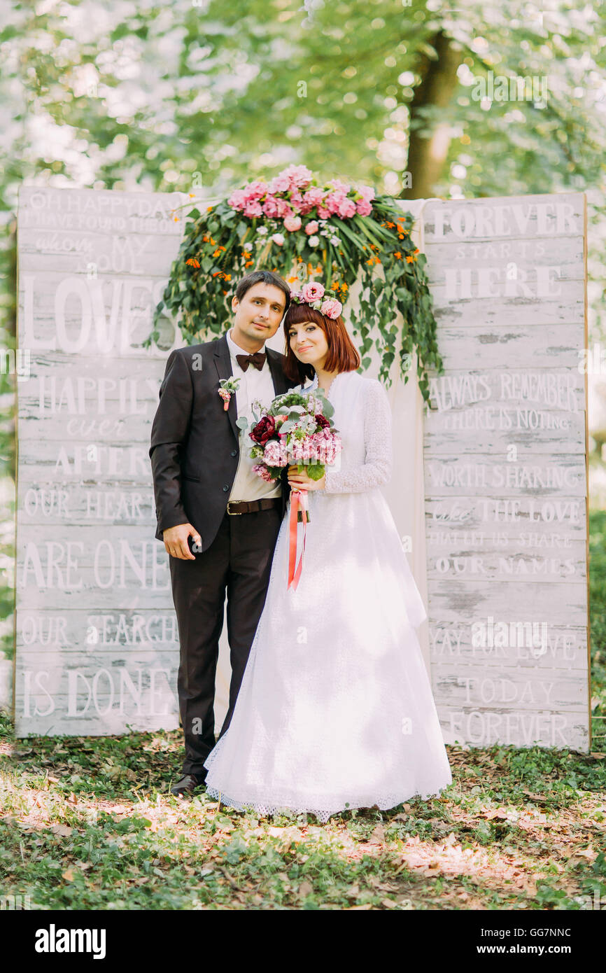 Charming bride and groom standing embracing near arch at wedding ...