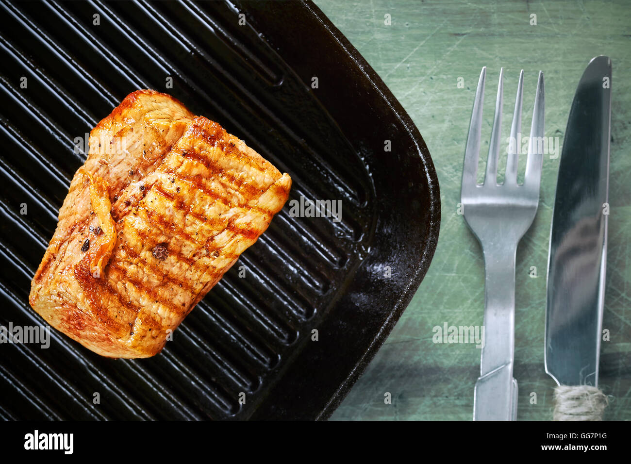 Close up picture of a roasted pork loin in black pan on wooden table. Stock Photo