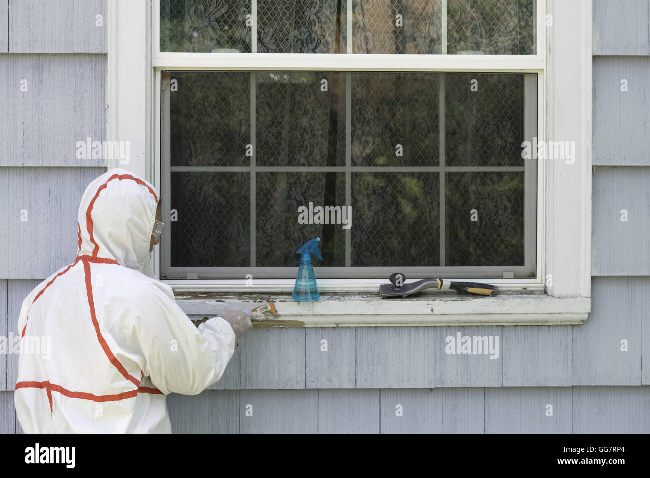 A house painter in a hazmat suit scrapes off dangerous lead paint from a window sill Stock Photo