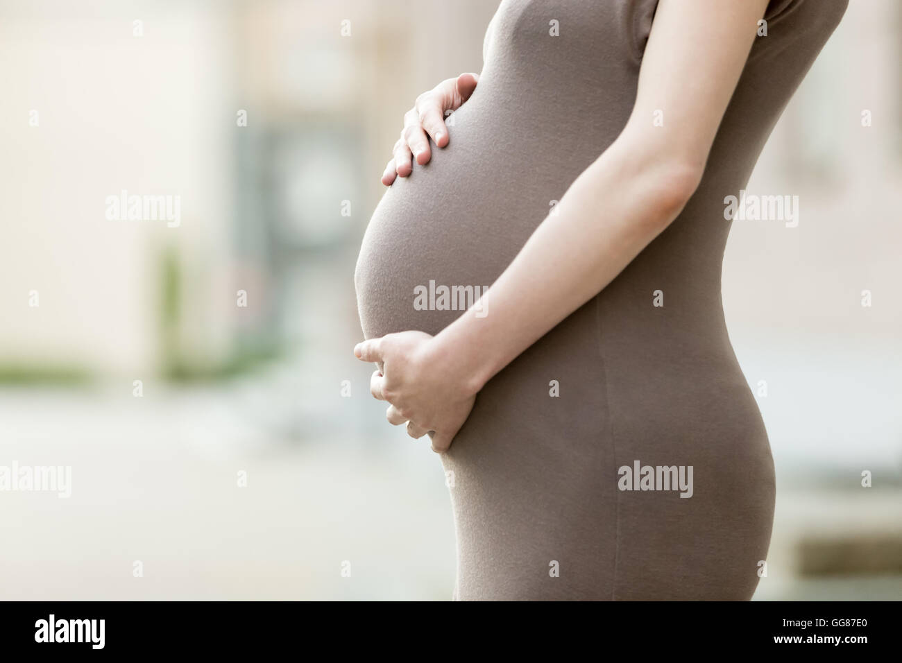 Love, family, healthy pregnancy concept. Close-up of belly of happy young pregnant woman standing on the street and caressing Stock Photo