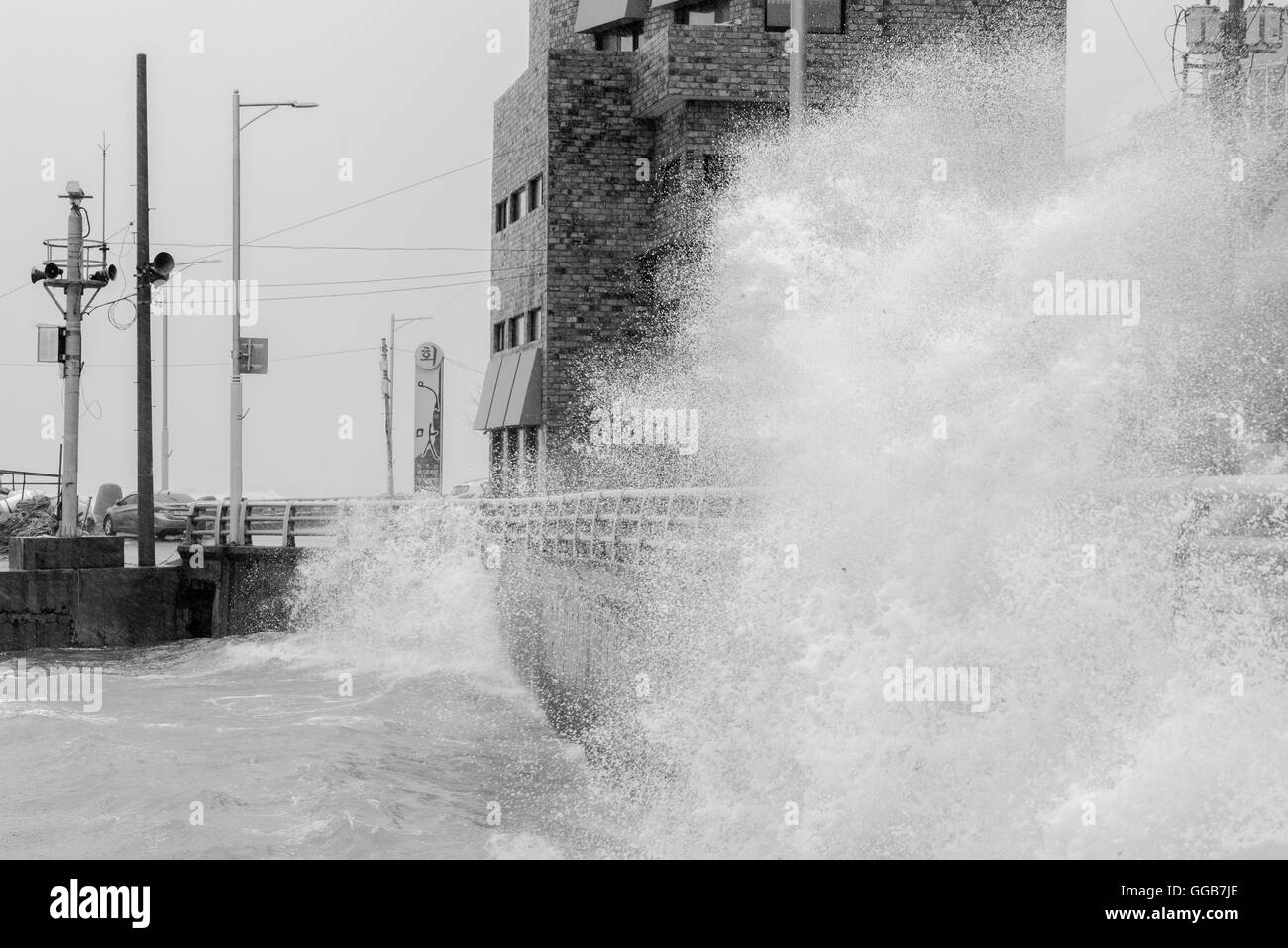 typhoon hitting small fishing village, big waves splashing, cresting, smashing near buildings B&W Stock Photo