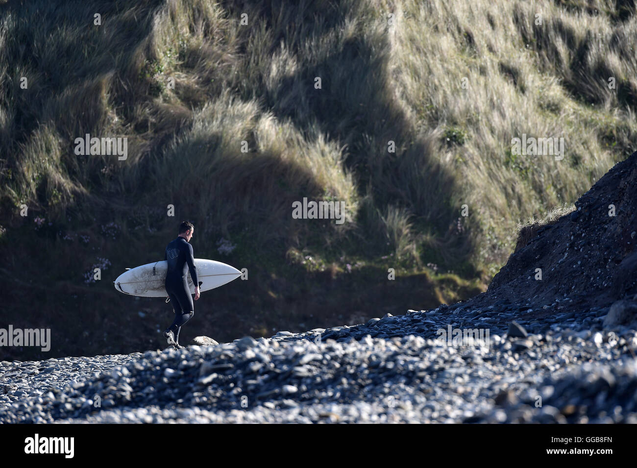 Surfer leaving the beach carrying surf board bathed in warm sunlight