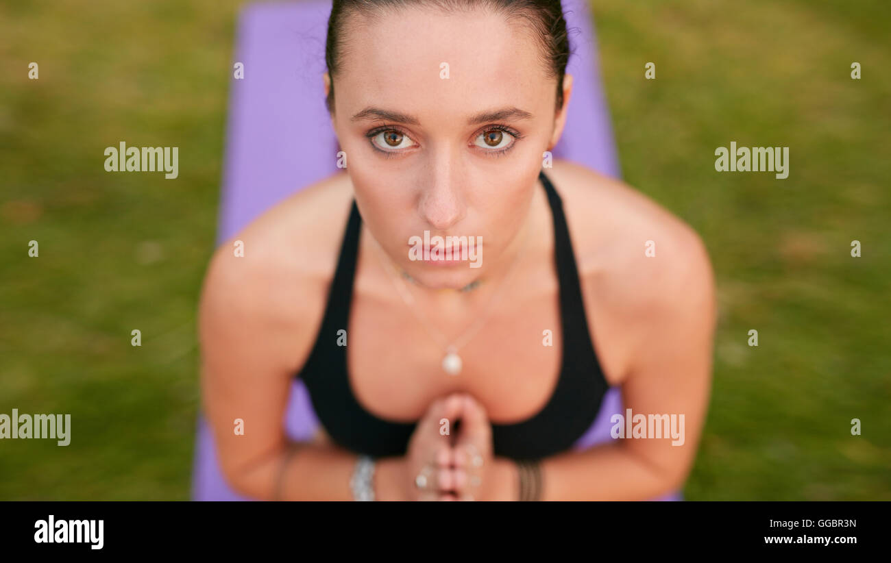 Close up shot of confident young woman meditating with clasped hands and looking at camera. Caucasian fitness female model pract Stock Photo