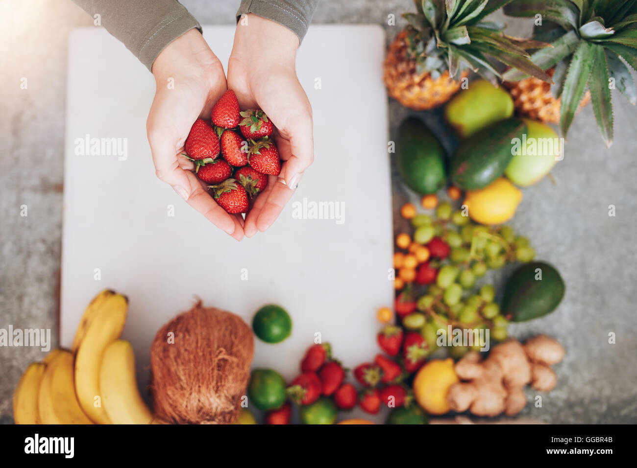 Top view shot of a female hands holding fresh strawberries over chopping board with fruits. Woman holding a handful of fresh str Stock Photo