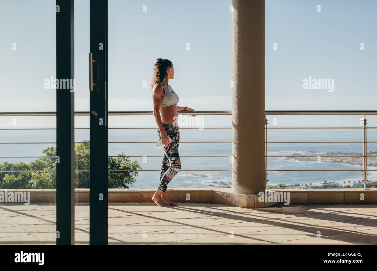 Outdoor shot of young woman standing in the balcony and looking at the view. Stock Photo