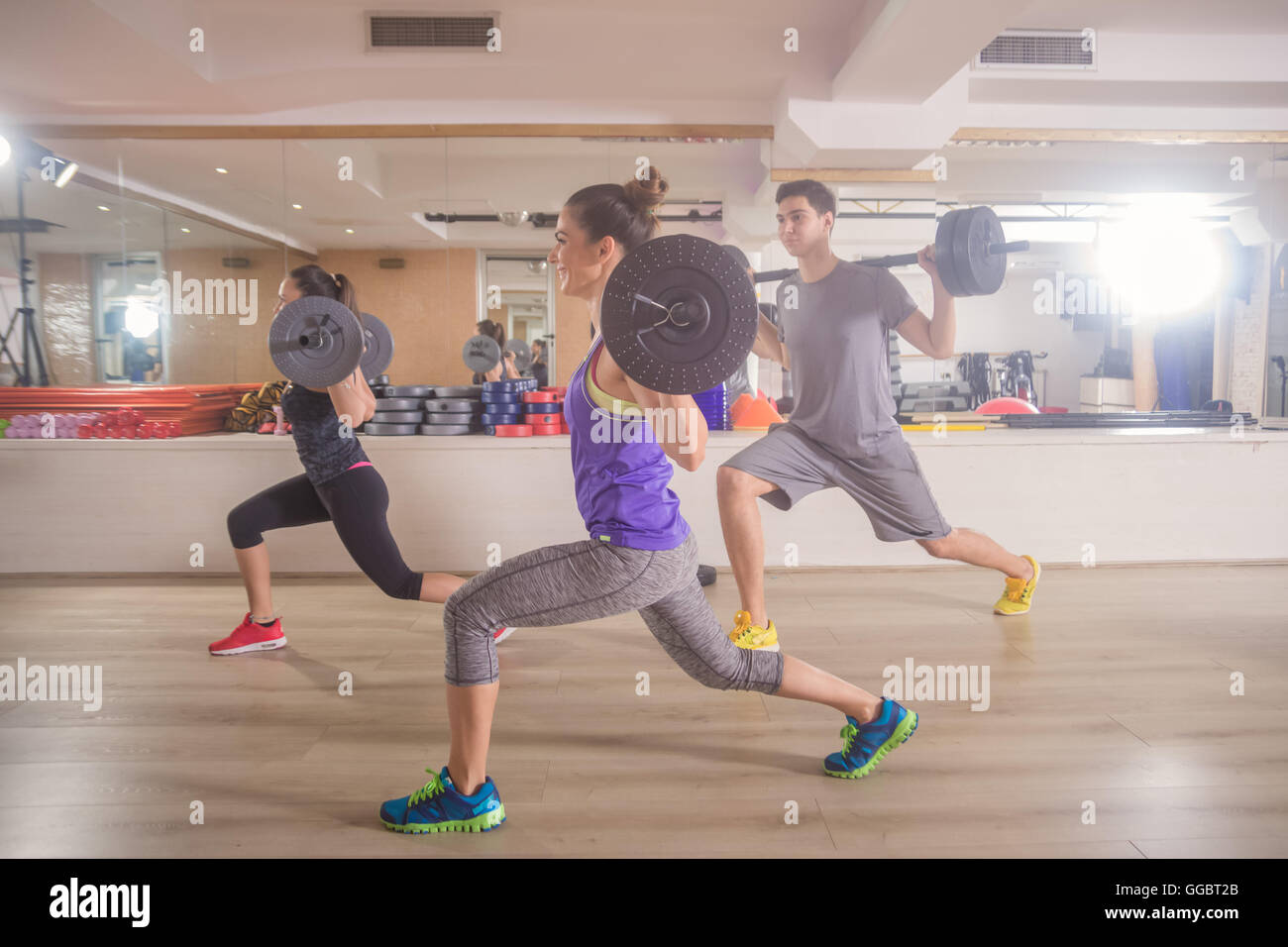 Three young people gym lunge weights bar women man Stock Photo