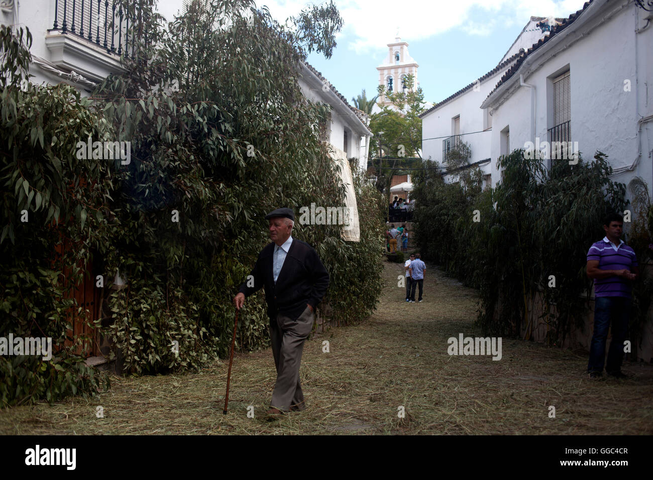 A senior man wearing a bonnet and using a walking stick walks in a street during Corpus Christi in El Gastor Stock Photo