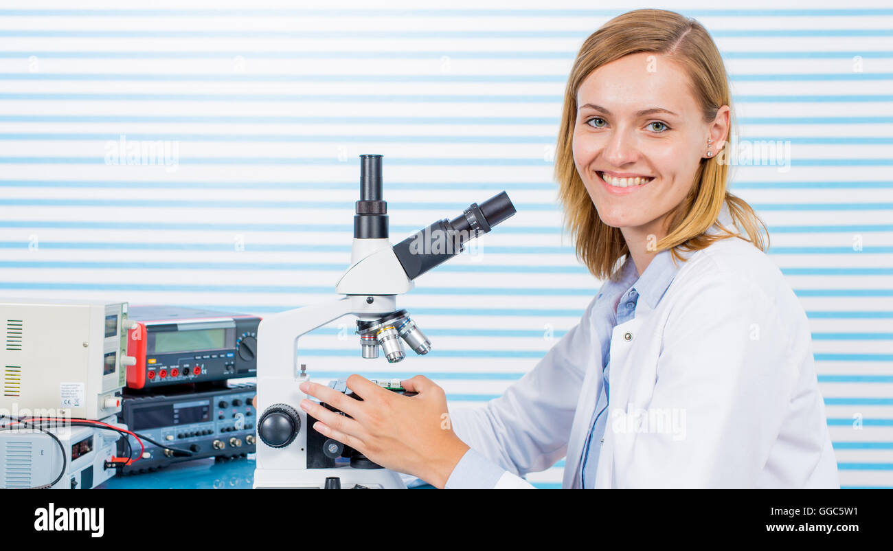 Young woman witch blonde long hair testing blood on RBC, HGB and HCT. laboratory bench which blood sample and microscope Stock Photo