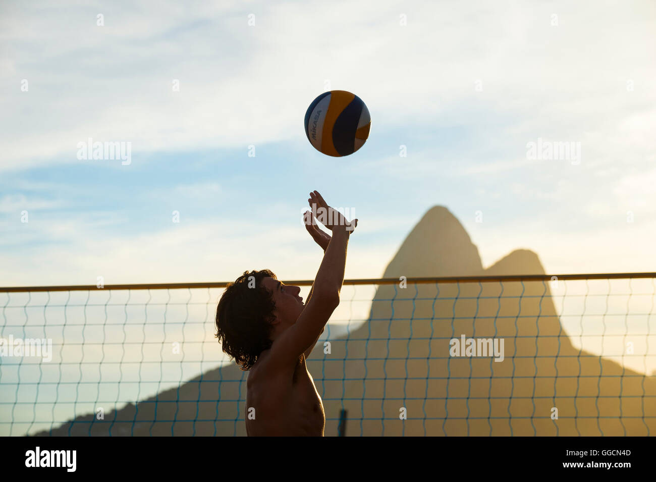 RIO DE JANEIRO - MARCH 20, 2016: Young Brazilian plays beach volleyball against a sunset silhouette of Two Brothers Mountain. Stock Photo