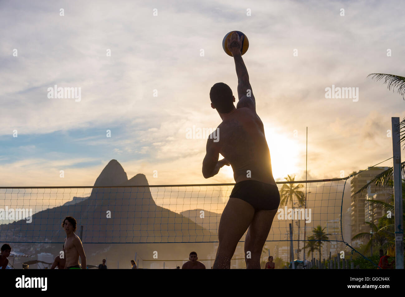 RIO DE JANEIRO - MARCH 20, 2016: Young Brazilian plays beach volleyball against a sunset silhouette of Two Brothers Mountain. Stock Photo