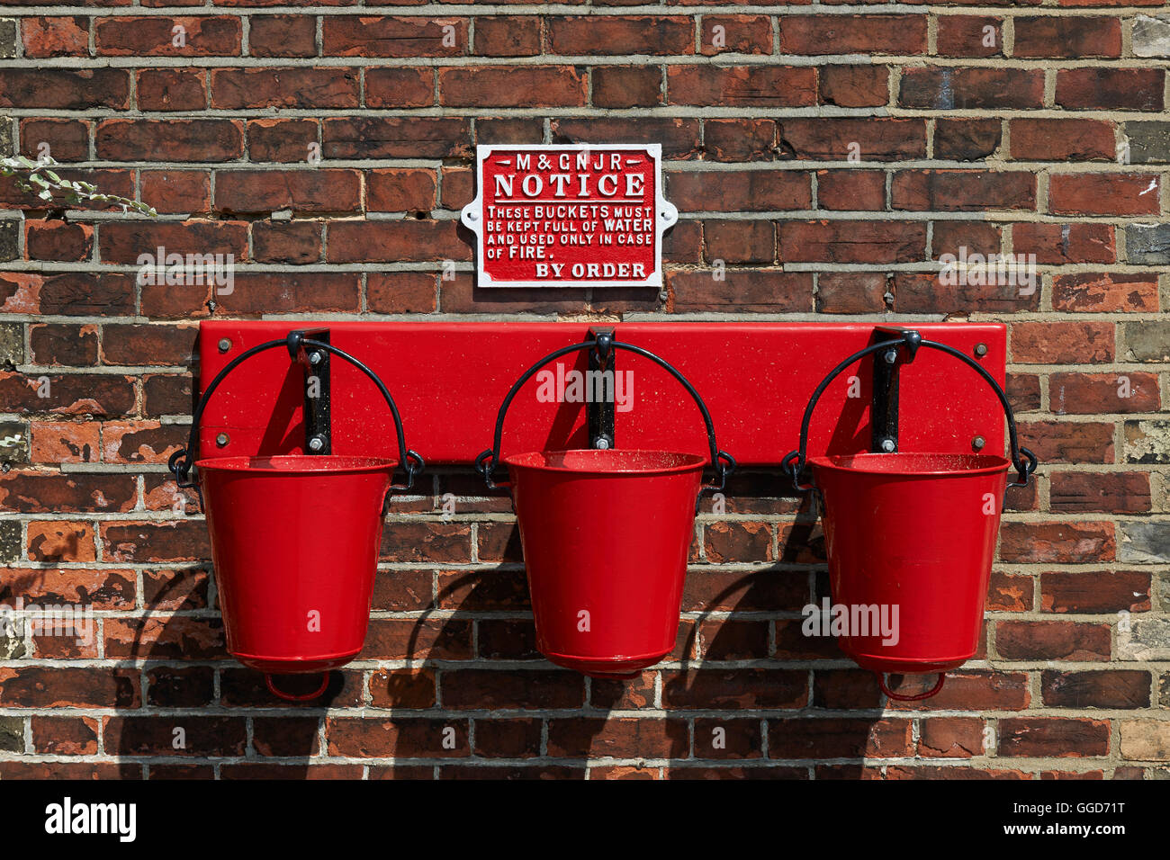 Red fire buckets hanging on hooks in a row of three, at an old 1940's railway station platform Stock Photo