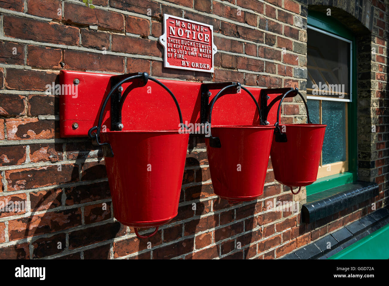 Red fire buckets hanging on hooks in a row of three, at an old 1940's railway station platform Stock Photo