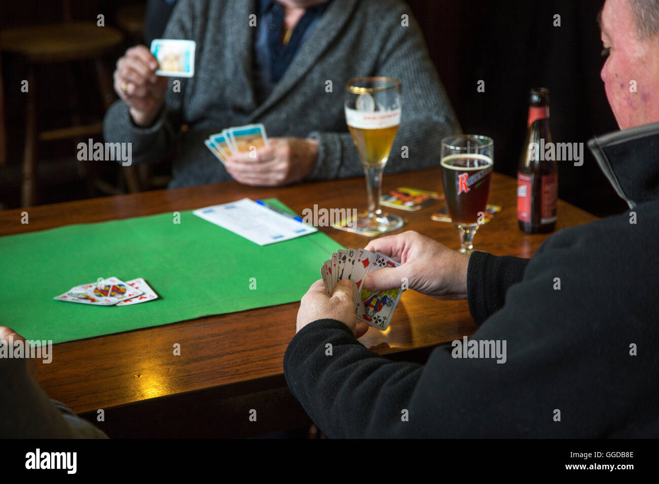 Elderly card players playing cards on table in pub Stock Photo