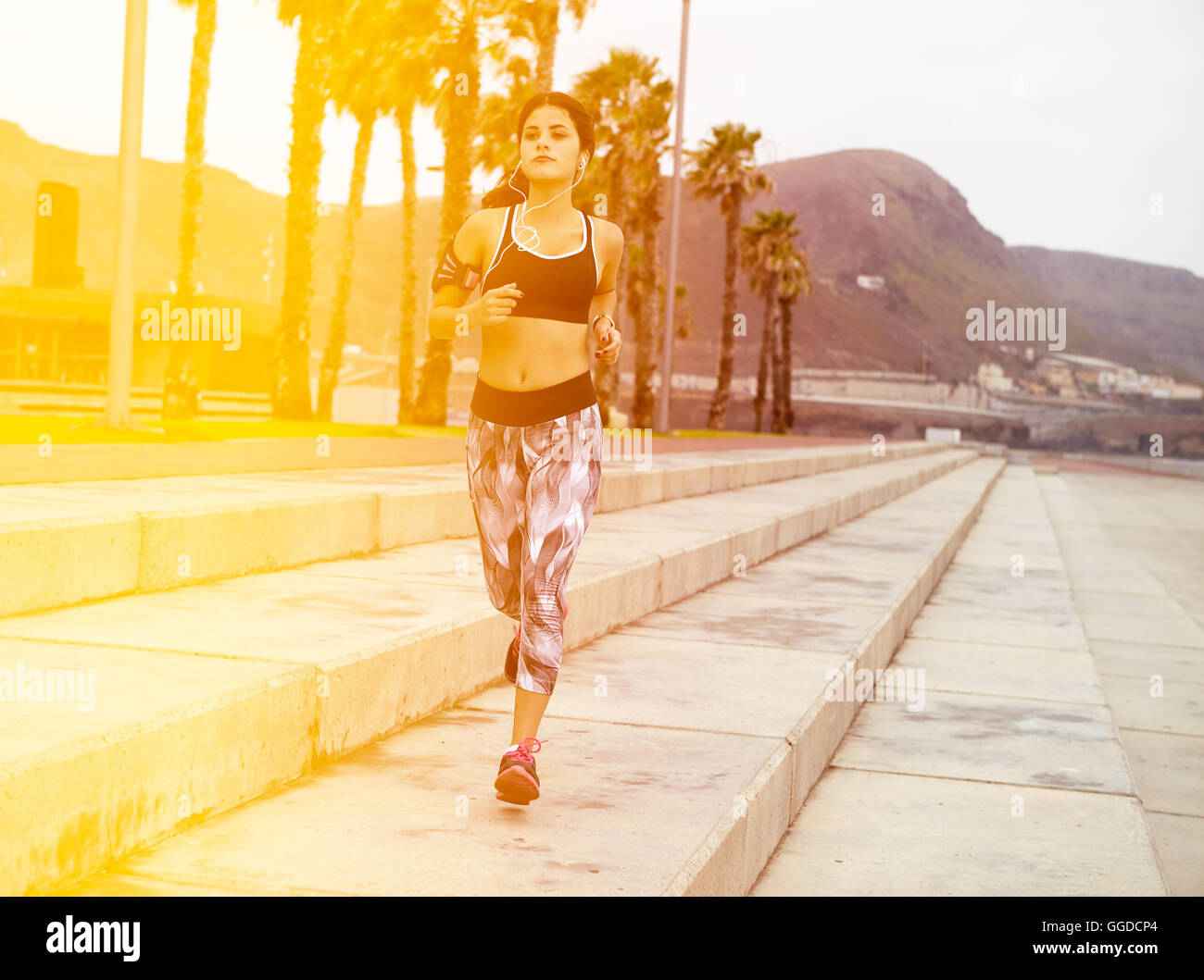 Young girl running on cement steps with palm trees behind her wearing casual clothes and her hair tied back Stock Photo