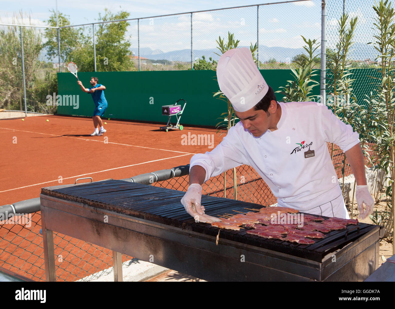 Cook putting meat on BBQ grill next to tennis court Stock Photo - Alamy