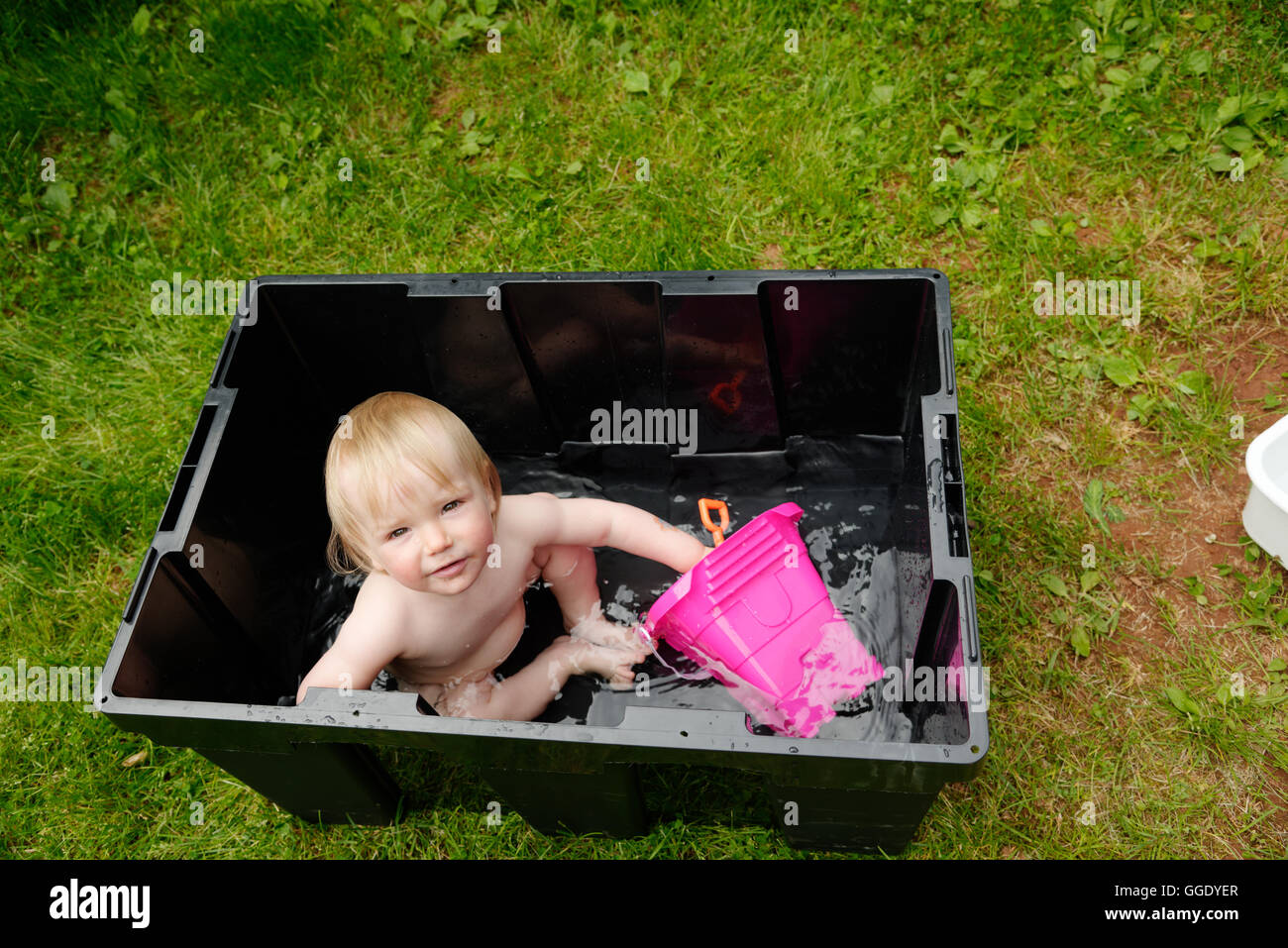 A little girl (2 years old) being bathed in a plastic box while camping Stock Photo