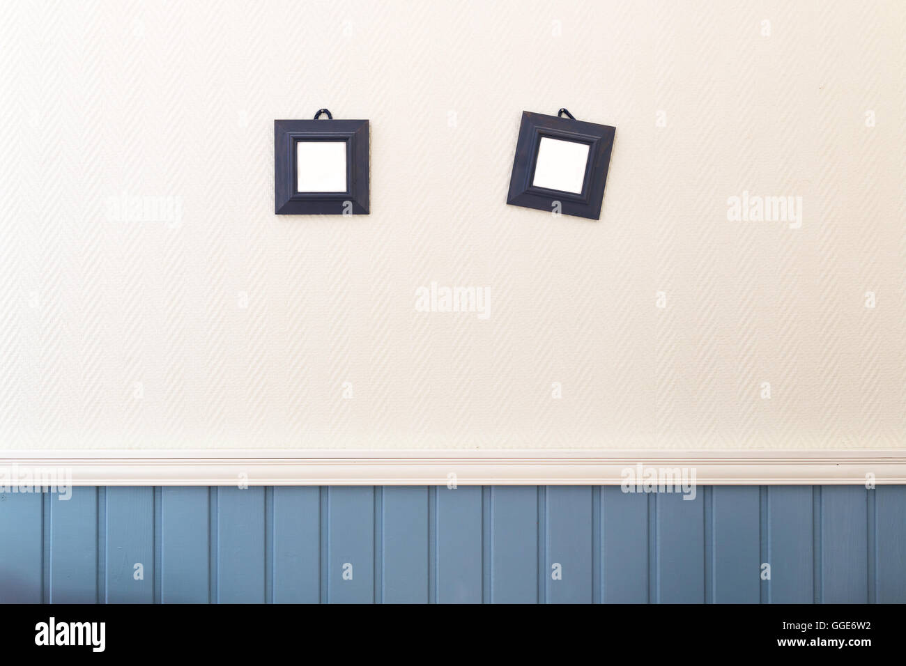 Two small square frames hanging on the white and blue wall. Stock Photo