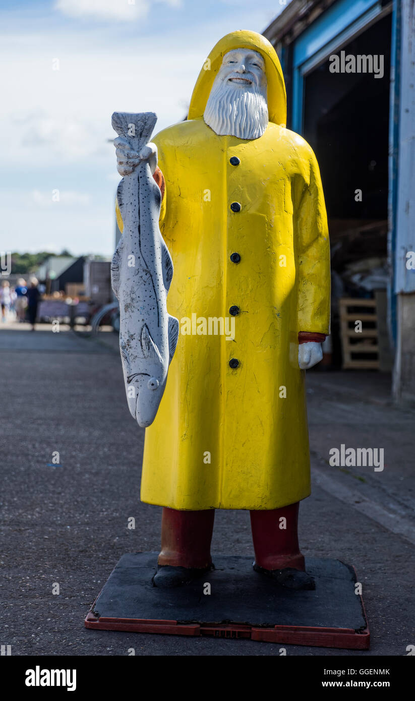A statue of a man holding a fish and wearing a souwester coat at Whitstable harbour in Kent Stock Photo