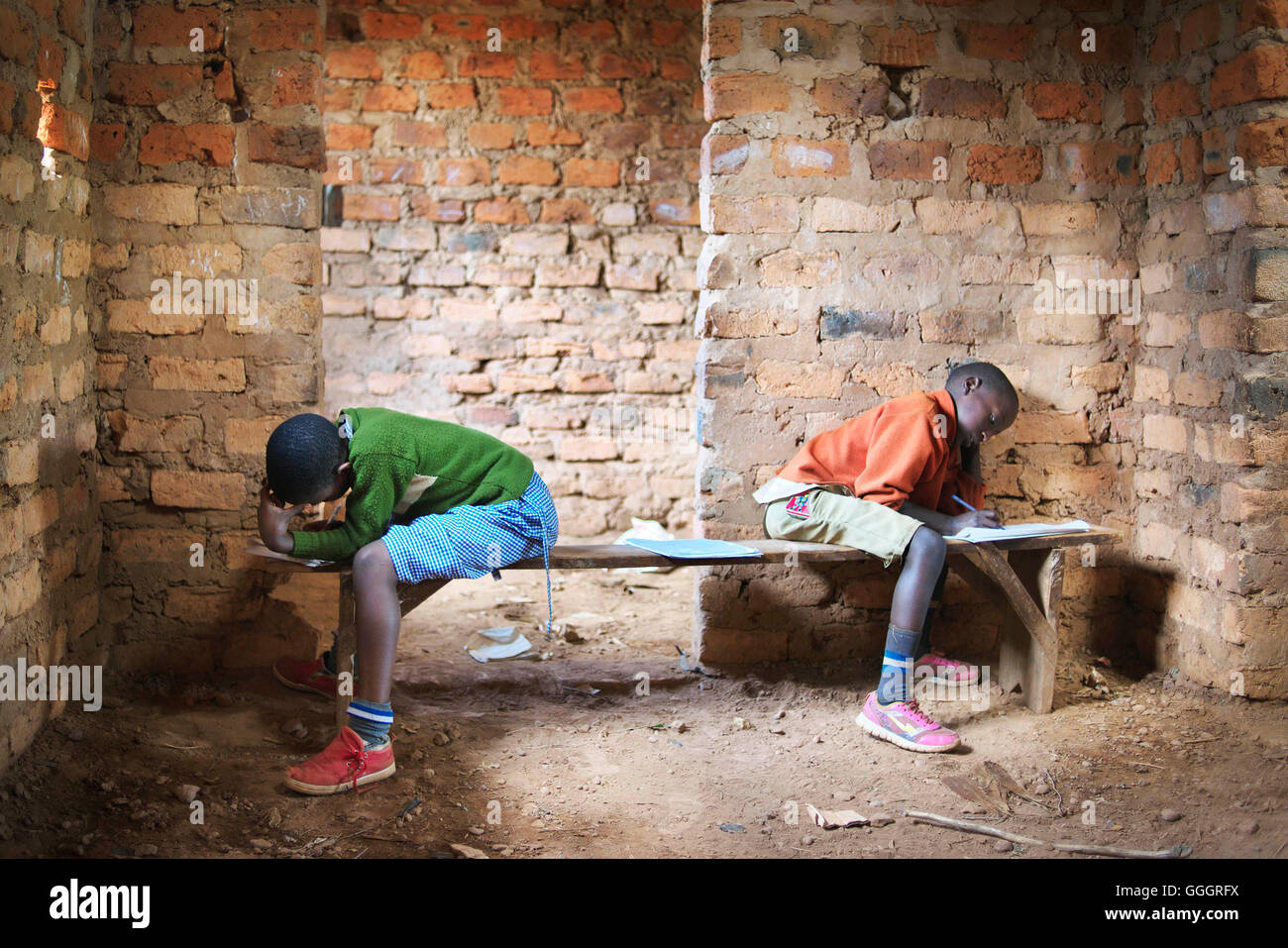 Two african school children in a rural school in Uganda/Rwanda take a school test, sitting opposite each other on wooden benches Stock Photo