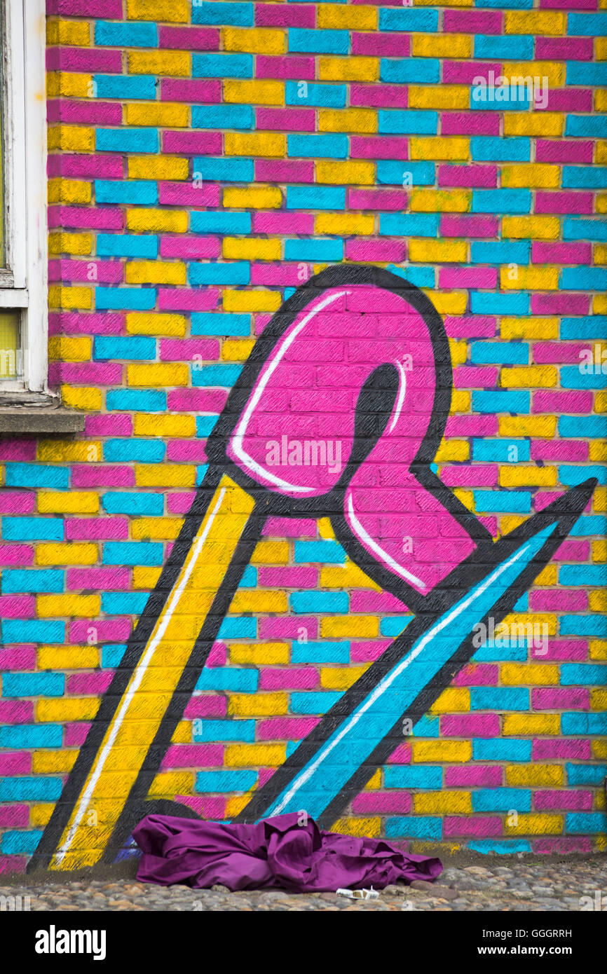 colourful mural graffiti of safety pin on wall with purple material and screwed up cigarette packet at Shoreditch, London Stock Photo