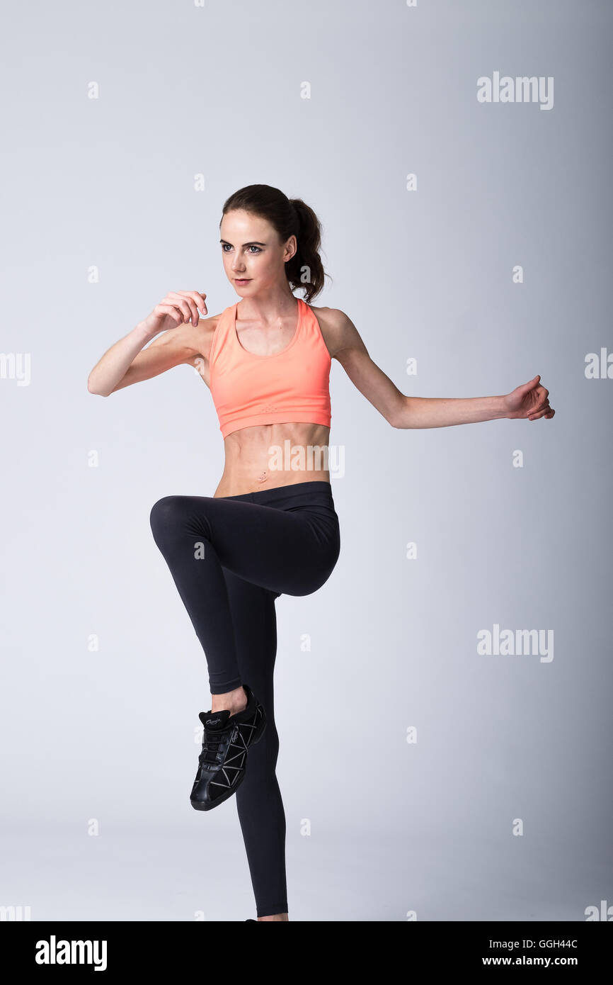 Woman in her 20s in fitness gear practising aerobics exercise moves on ...