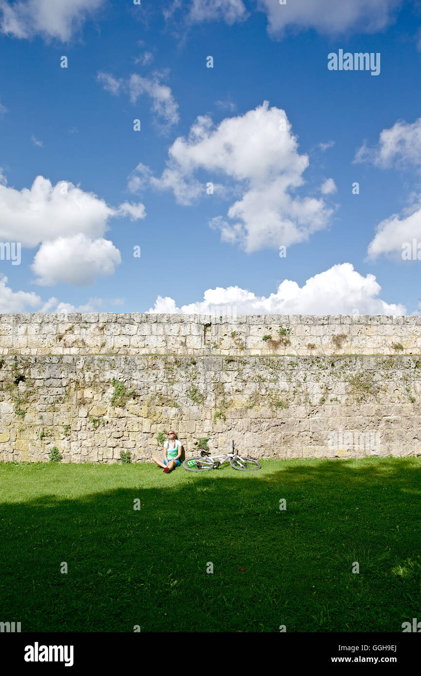 Female cyclist resting at castle wall, Burghausen, Chiemgau, Bavaria, Germany Stock Photo