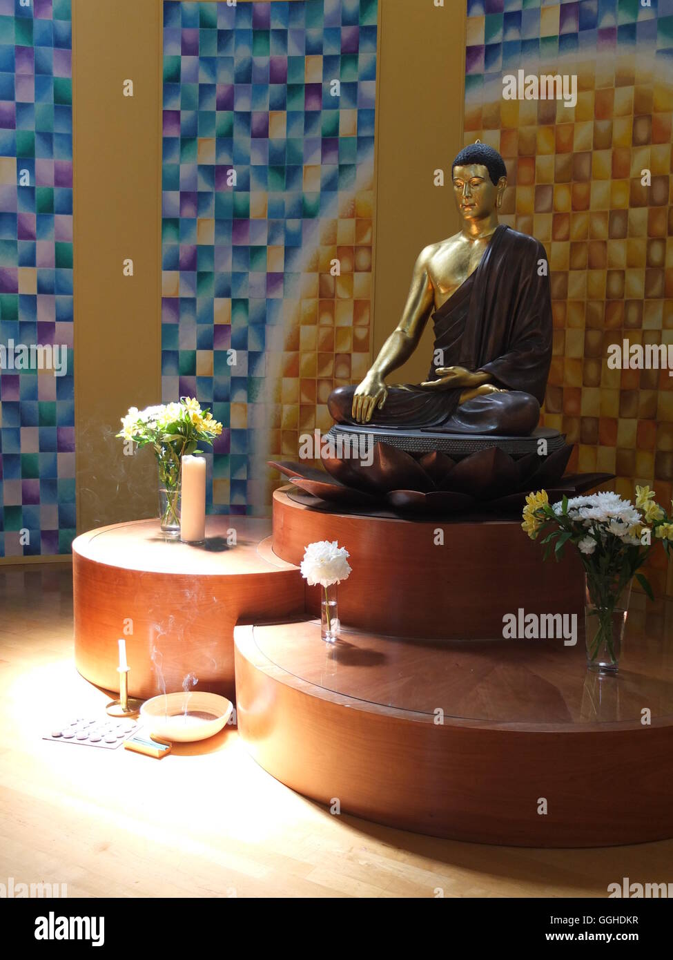A statue of Buddha, candles, vases of flowers and some burning incense