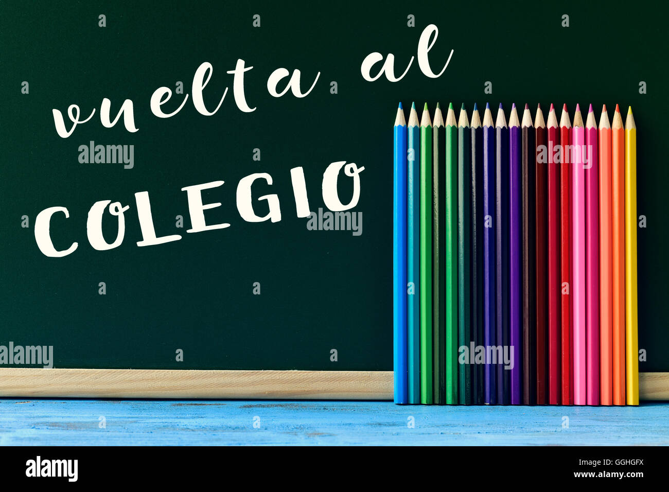 text vuelta al colegio, back to school in spanish written in a chalkboard and some new pencil crayons of different colors put in Stock Photo