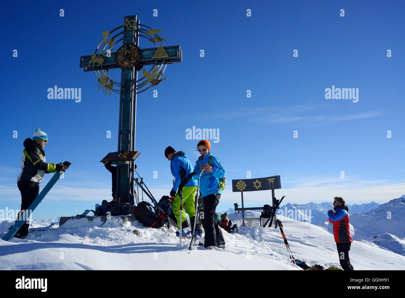 Back-country skiers beside a summit cross with signs of world religions, Kleiner Gilfert, Tux Alps, Tyrol, Austria Stock Photo