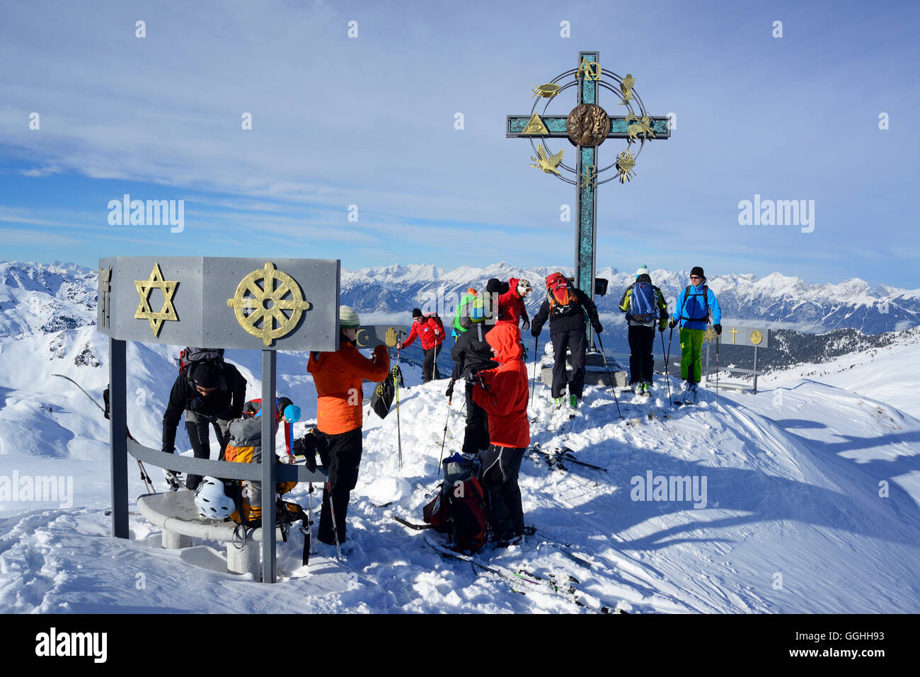 Back-country skiers beside a summit cross with signs of world religions, Kleiner Gilfert, Tux Alps, Tyrol, Austria Stock Photo