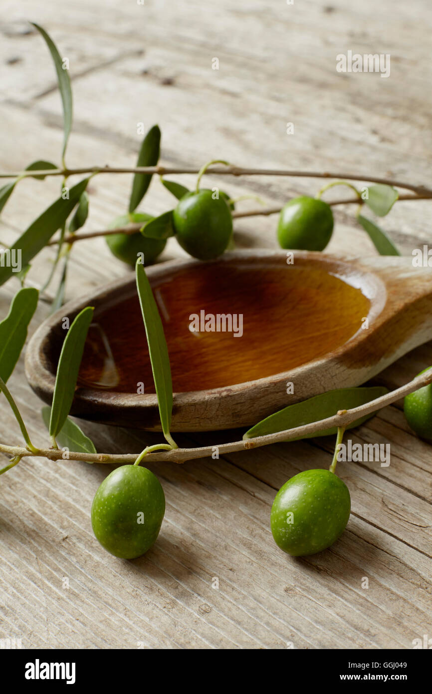 Green olive branch and a spoon full of oil on the wooden table Stock ...