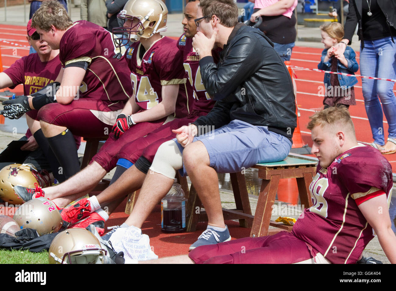 Ipswich Cardinals players watch from the sideline seated on a bench Stock Photo