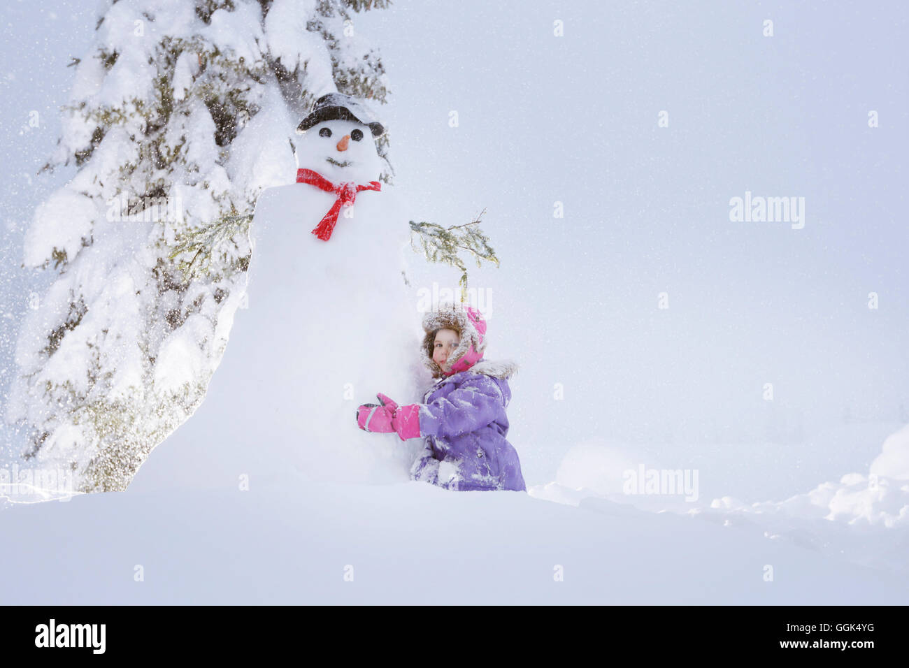 Girl crouching beside a snowman, Passo Monte Croce di Comelico, South Tyrol, Italy Stock Photo