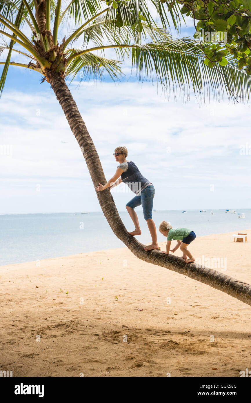 Mother and son climbing on a coconut tree, walking, beach, little boy 3 years old, western family, family travel in Asia, parent Stock Photo