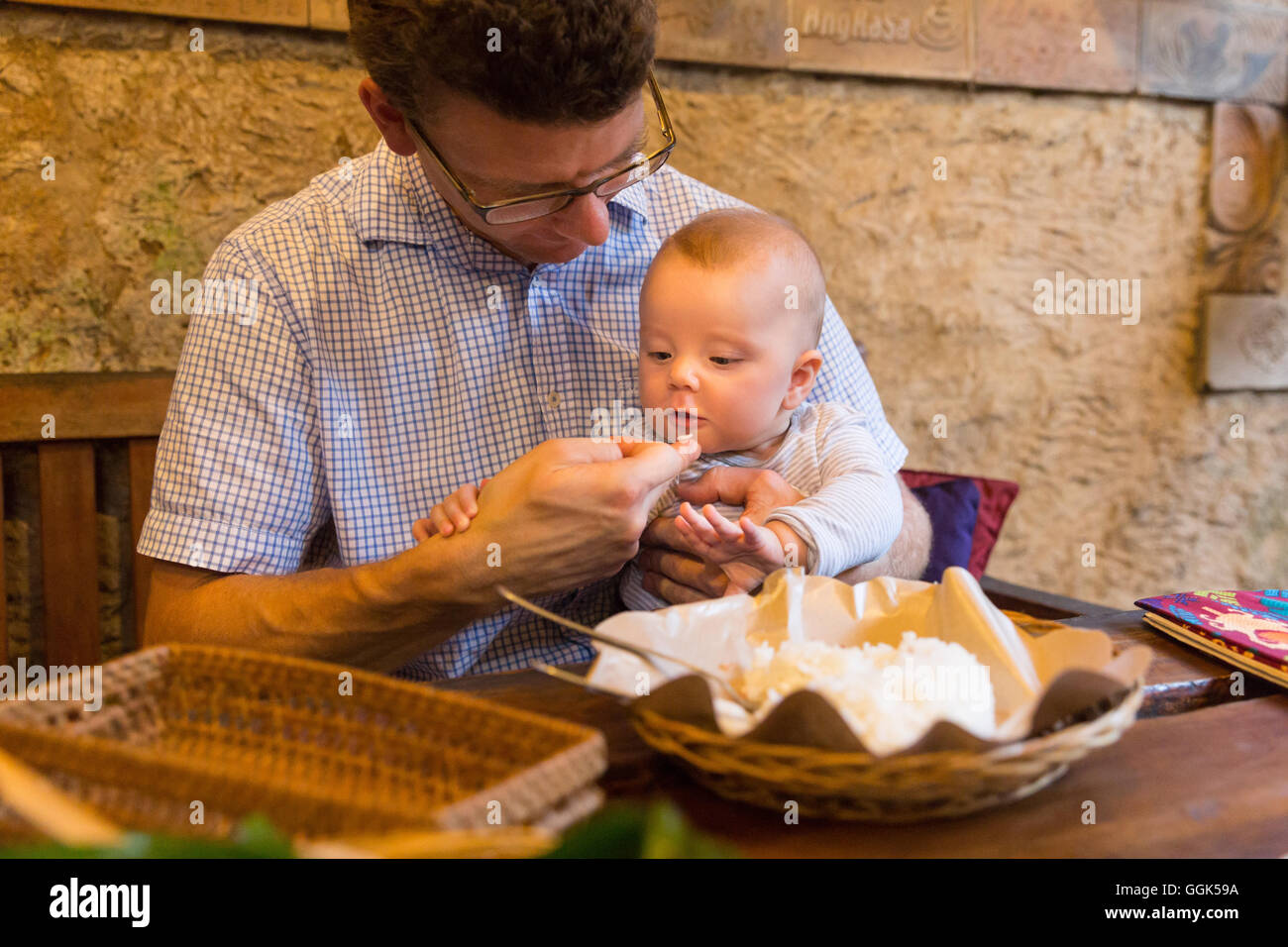 Father and daughter eating in a restaurant, baby trying her first rice, grain, traditional Balinese food, restaurant Biah Biah, Stock Photo