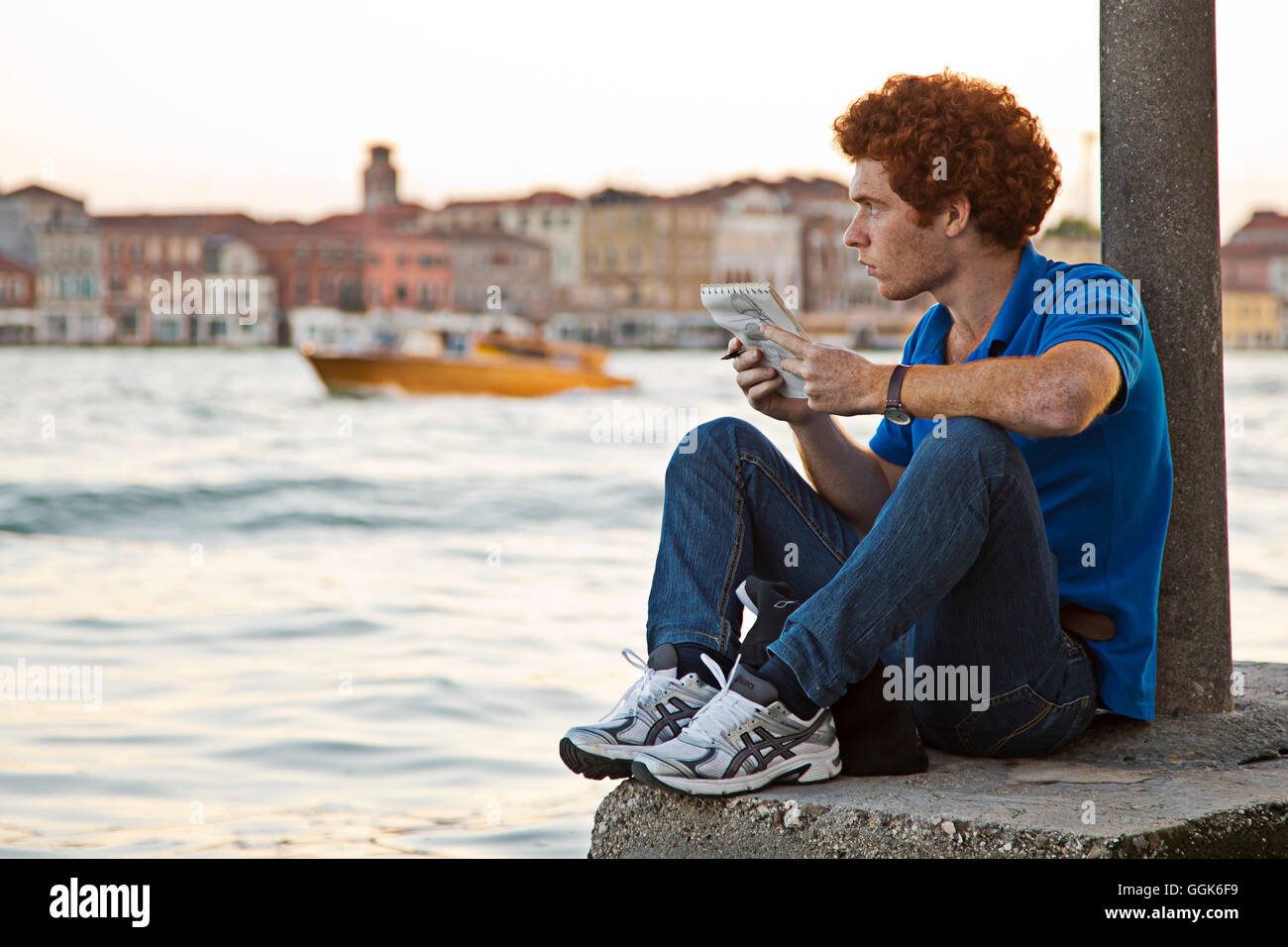 A red-haired young man sitting on the banks of the Canale della Giudecca in Dorsoduro drawing, Venice, Veneto, Italy, Europe Stock Photo