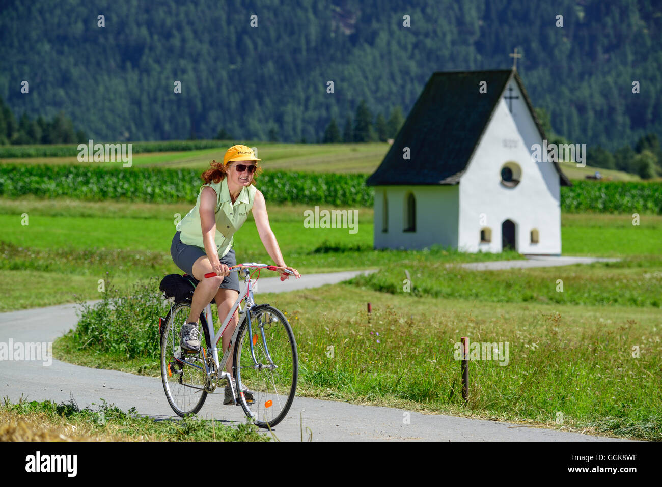 Woman cycling along Inn cycle route, chapel in background, Karres, Tyrol, Austria Stock Photo