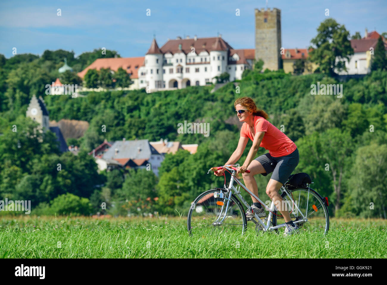 Woman cycling, Neubeuern castle in background, Neubeuern, Upper Bavaria, Bavaria, Germany Stock Photo