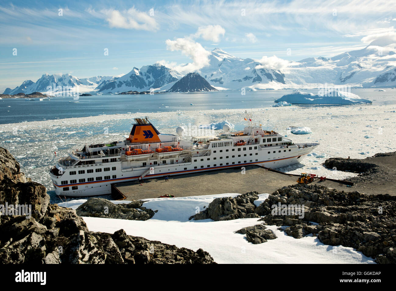 Expedition cruise ship MS Hanseatic (Hapag-Lloyd Cruises) moored at the concrete pier with icebergs and mountains in the distanc Stock Photo