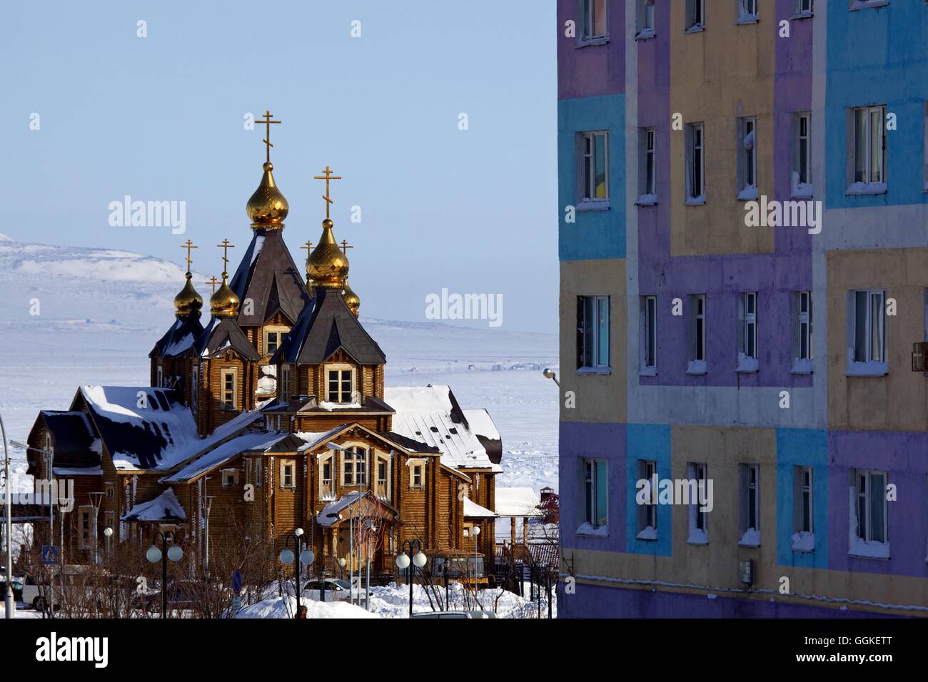 Orthodox Cathedral of the Holy Trinity next to coloured apartment house, Anadyr, Chukotka Autonomous Okrug, Siberia,  Russia Stock Photo