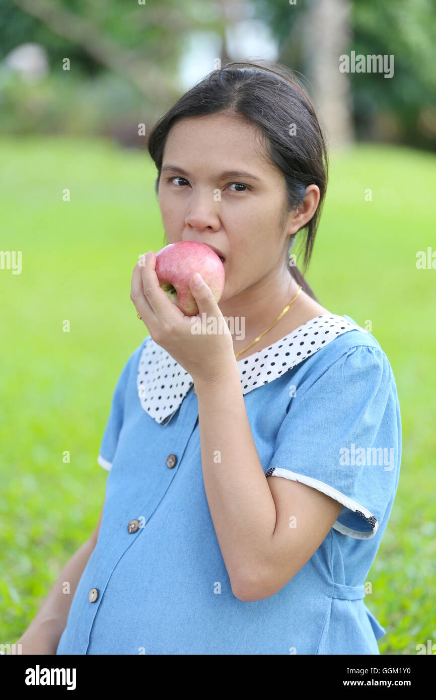 Asian pregnant women using hand catch apple up eating in the public park. Stock Photo