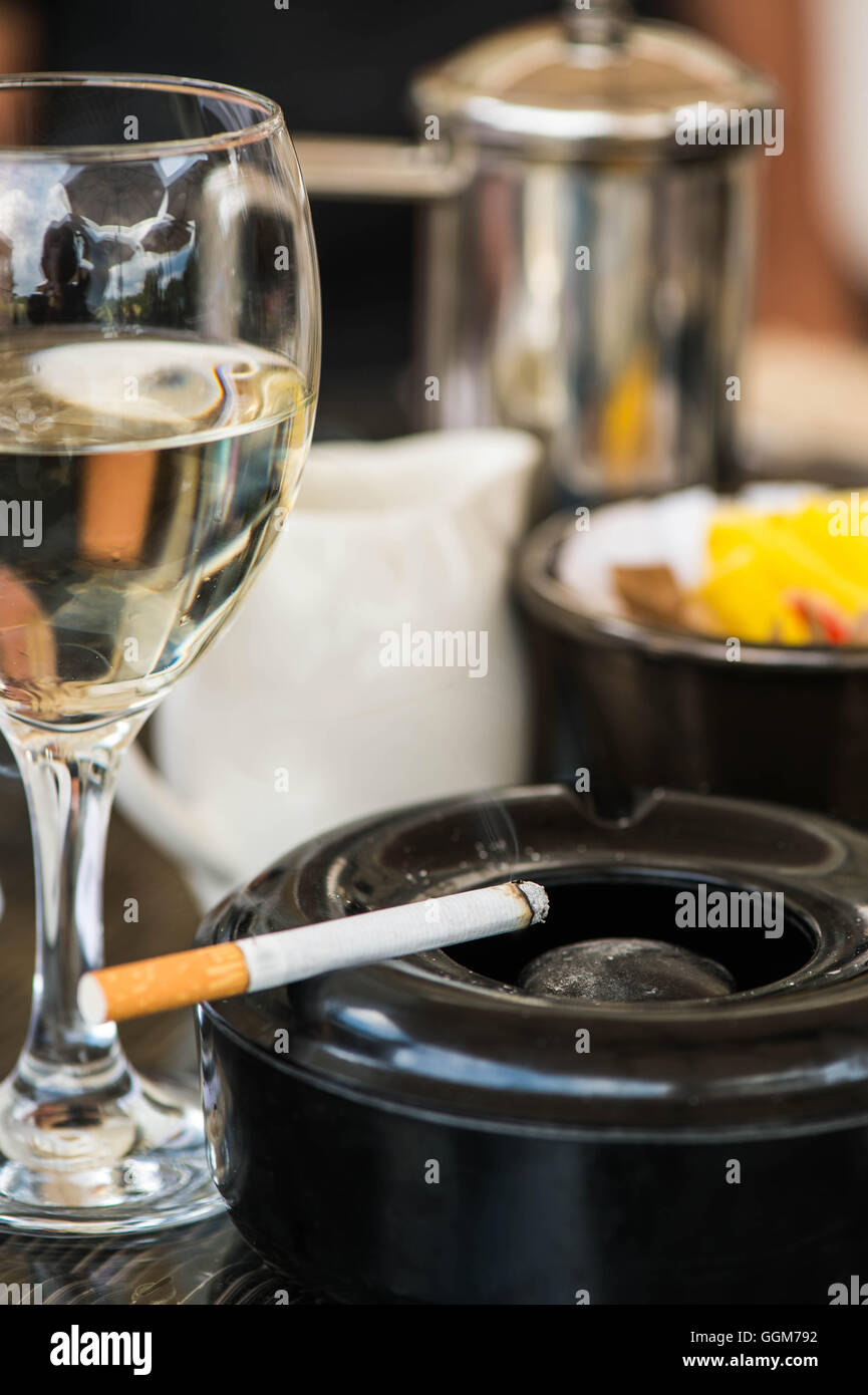 Glass Of Chilled White Wine With Ashtray And Lit Or Burning Cigarette, On Table Top Setting, In Cafe Or Restaurant With No People Stock Photo