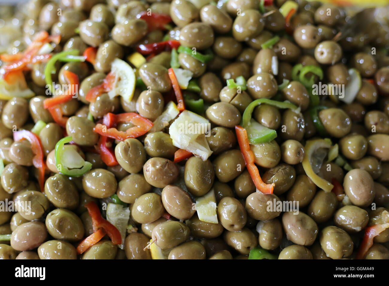 Green Olives. Green spicy olives in a market stall, close up. Stack of brown olives decorated with red and green bell pepper slices and yellow lemon p Stock Photo