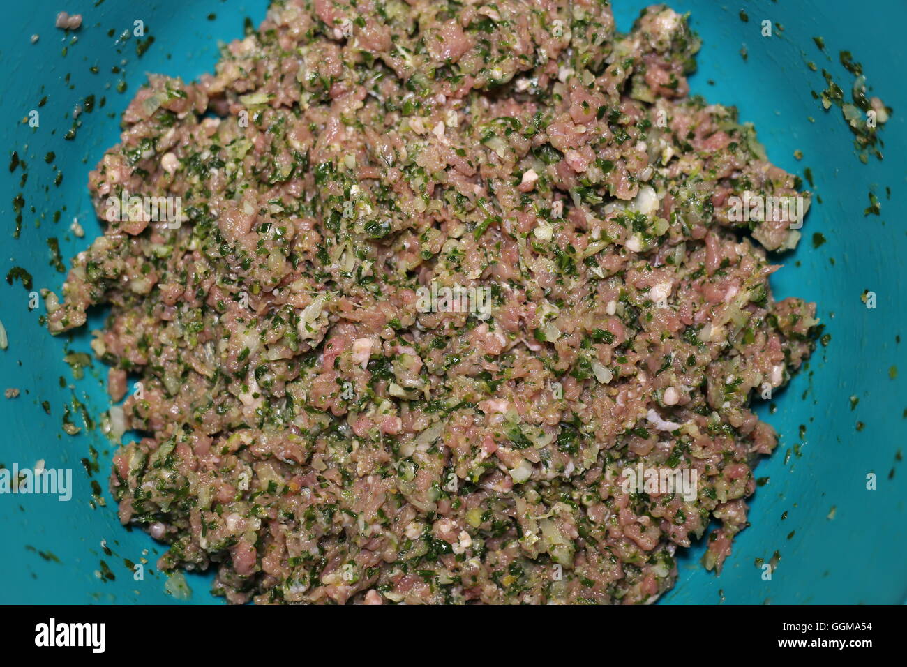 Minced Meat Mix. Not for vegetarians: Raw minced beef meat mixed with spinach, onion and spices in a green plastic bowl for meatballs or hamburger Stock Photo