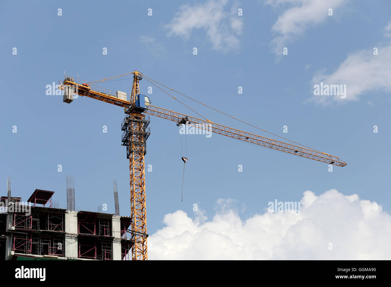 Crane working on a building under construction in day time and blue sky background. Stock Photo