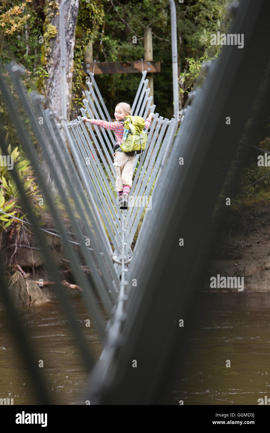 A girl traversing a rope bridge, a walk wire at Lake Manapouri, Fjordland, South Island, New Zealand Stock Photo